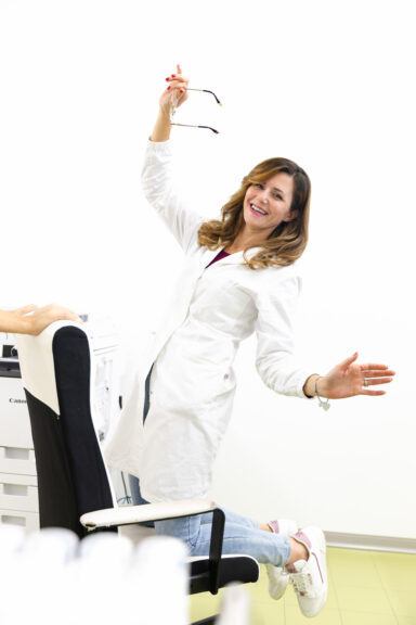 Fondatrice di Cosmetu con camice bianco che sorride e salta accanto alla poltrona in laboratorio, immagine dinamica del team del brand cosmetico