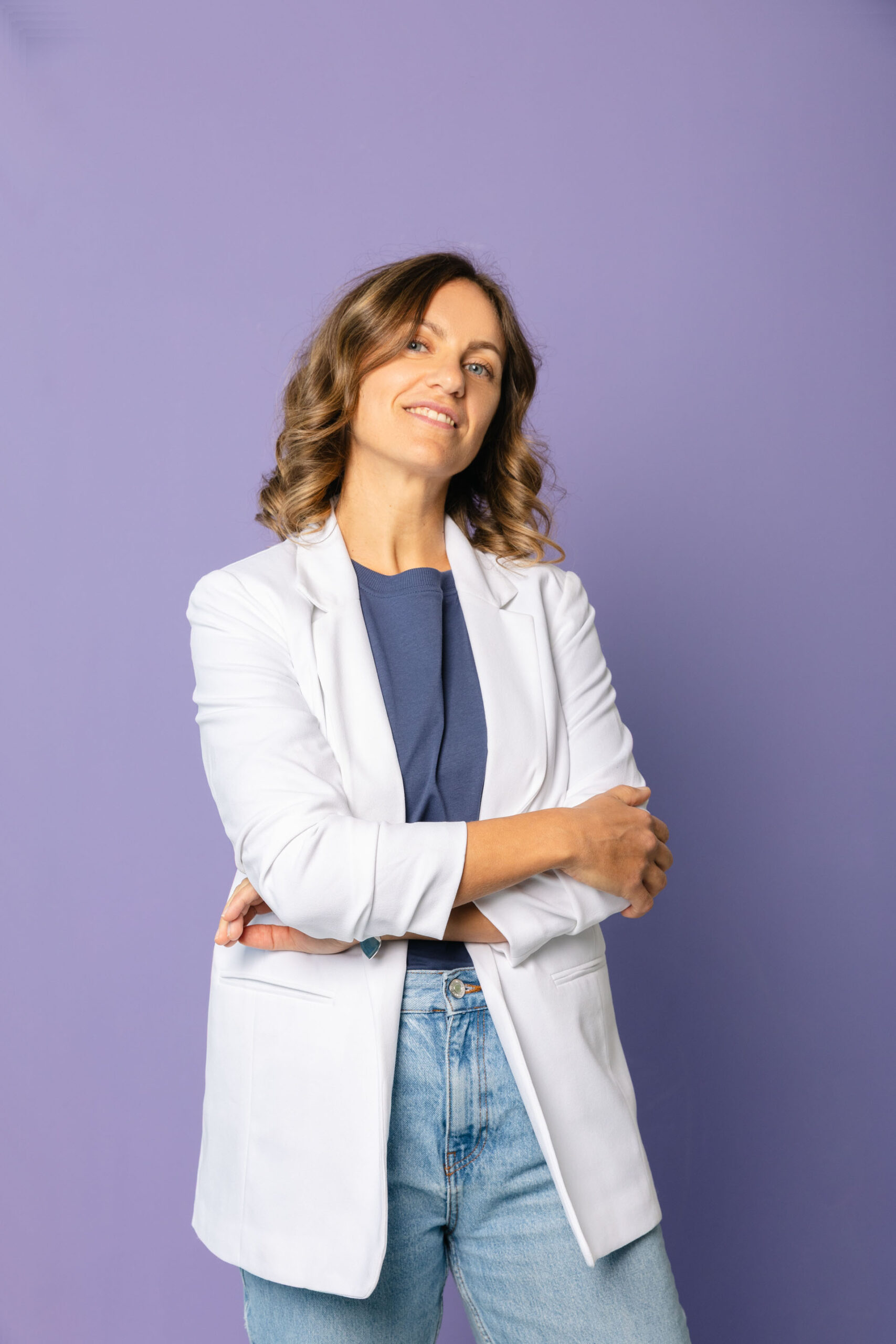 Terza cofondatrice di Cosmetu con camice chiaro e braccia conserte su sfondo lilla, ritratto per la pagina Chi siamo del brand di cosmetica