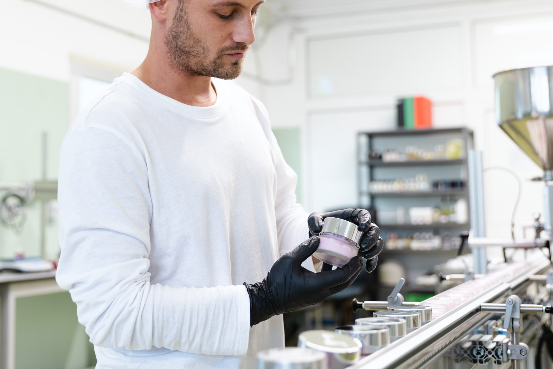 Operatore specializzato che esegue il controllo qualità su un vasetto di crema cosmetica in fase di confezionamento.